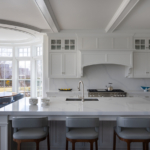Bright kitchen island with sink; chairs, range, bay window.